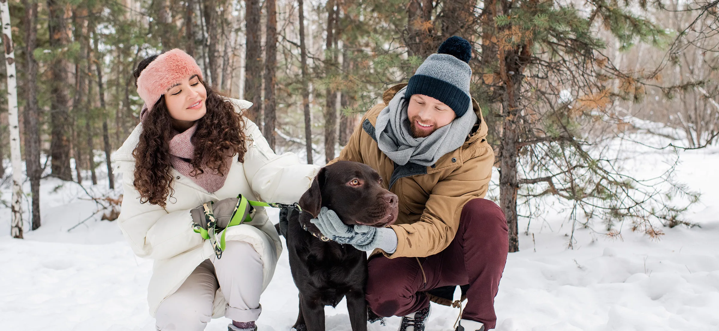 Couple with dog dressed for winter outside in the snow.