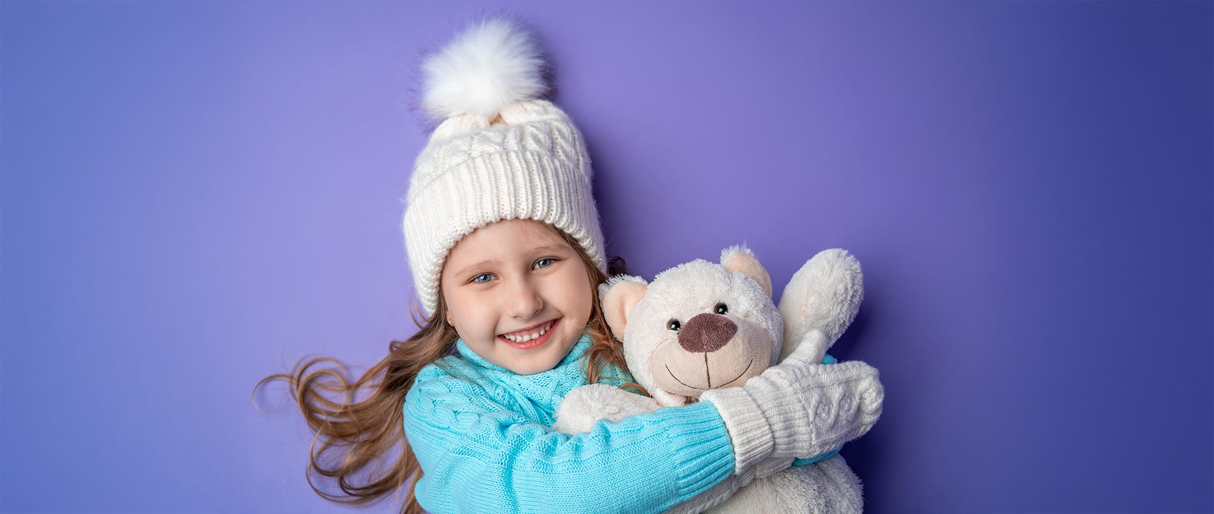 Girl wearing winter hat and mittens holding a white bear on a purple background.