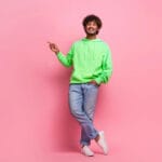 Man in green hoodie and jeans on a pink background.