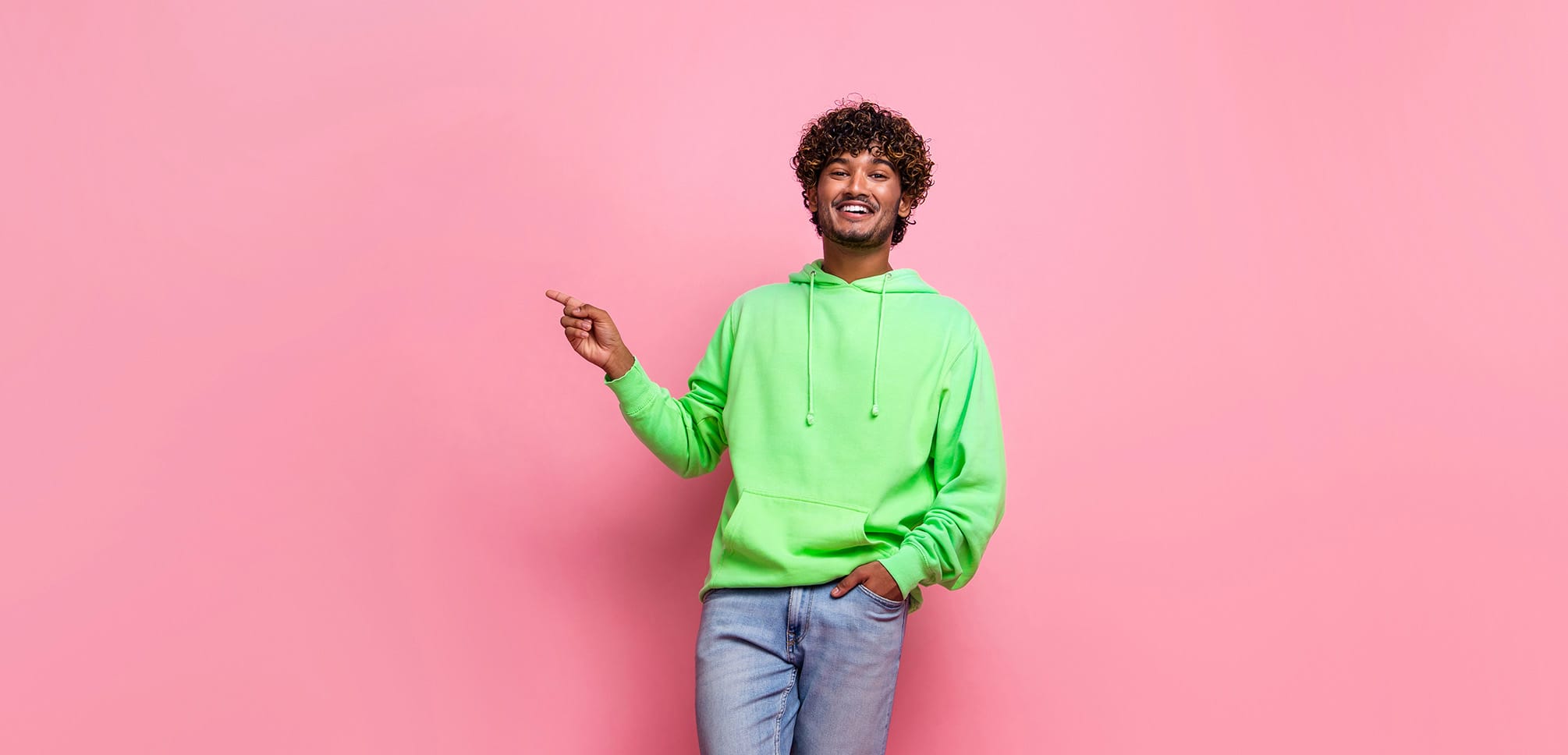Man in green hoodie and jeans on a pink background.