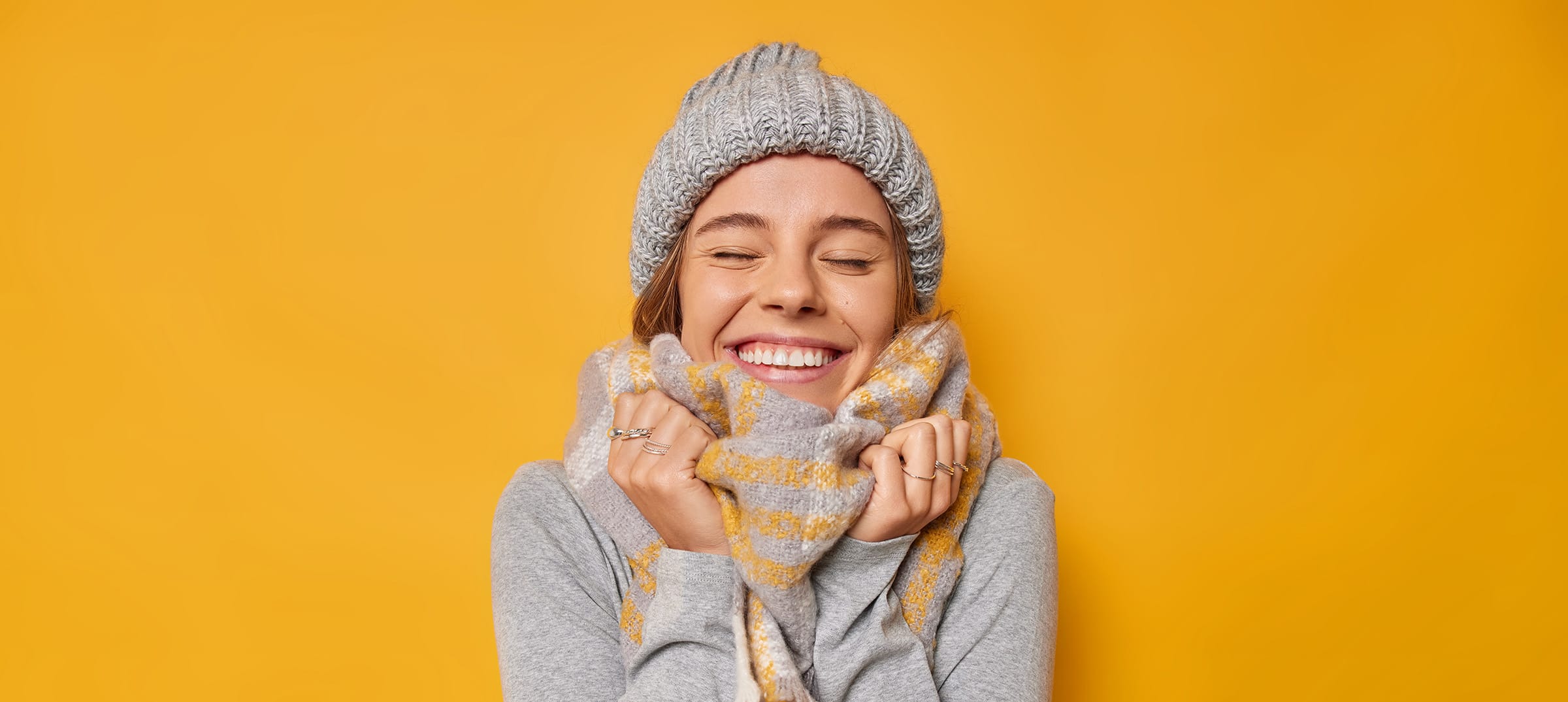 Woman wearing winter hat and scarf on yellow background.
