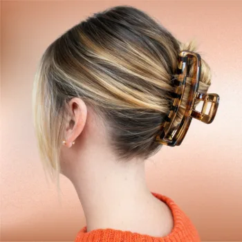 Blonde hair styled in a low twist secured with a tortoise shell rectangular claw clip against a soft peach background.