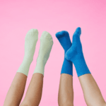 Two pairs of crew socks in mint green and bright blue worn on raised legs against a pink background.